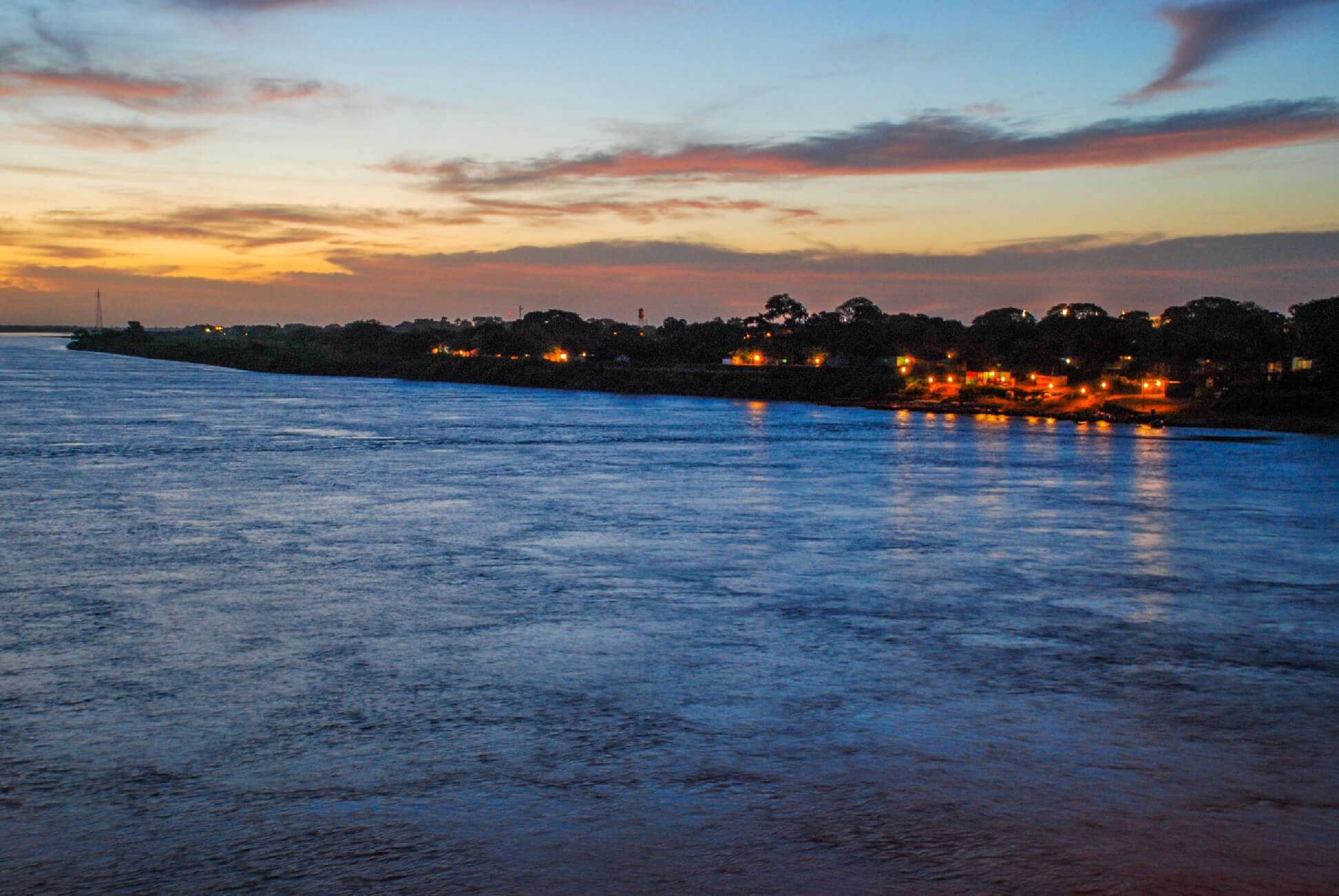 Paisaje sereno de un río al atardecer con luces en la orilla.