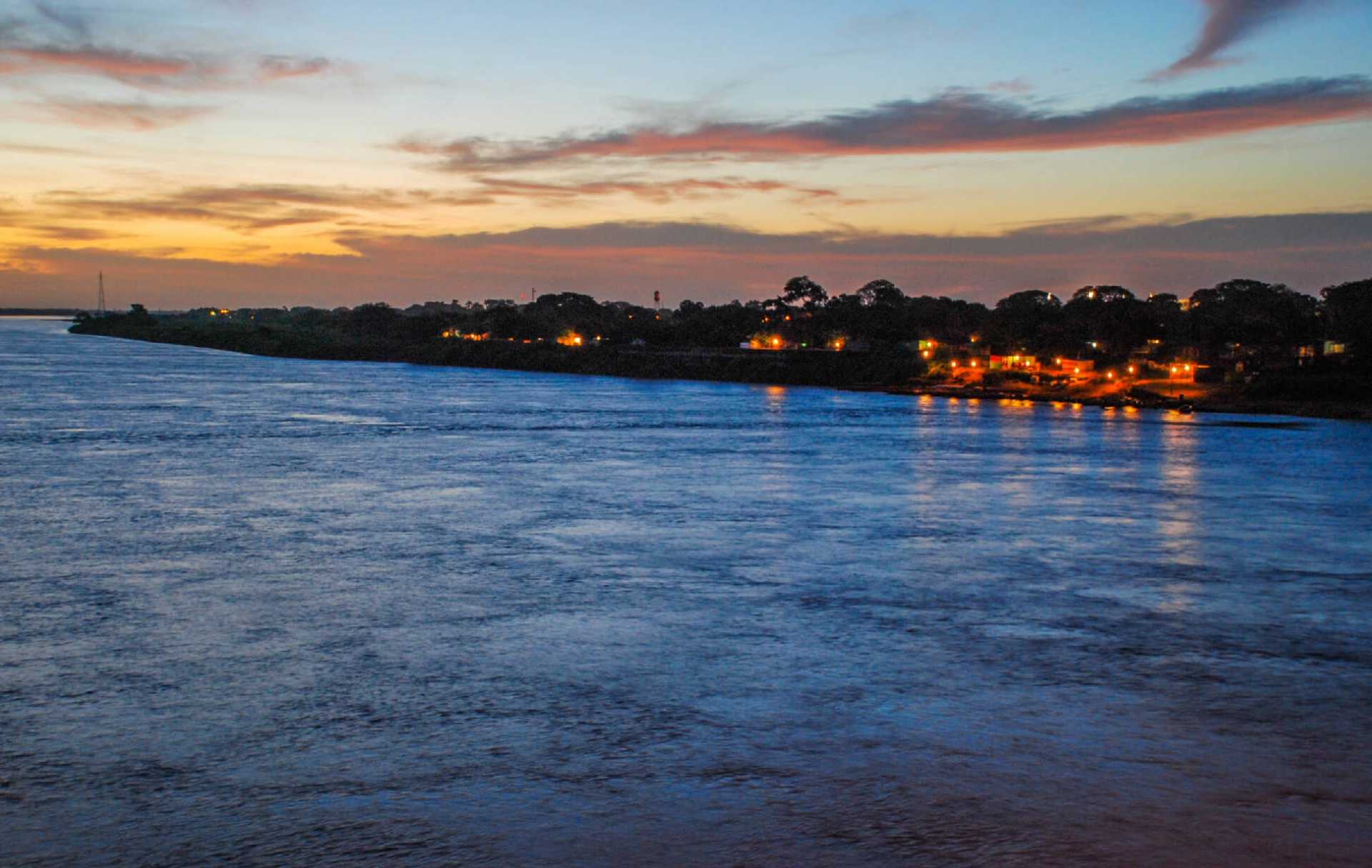 Vista del río Orinoco al atardecer en Puerto Carreño, Colombia, con luces de la ciudad.