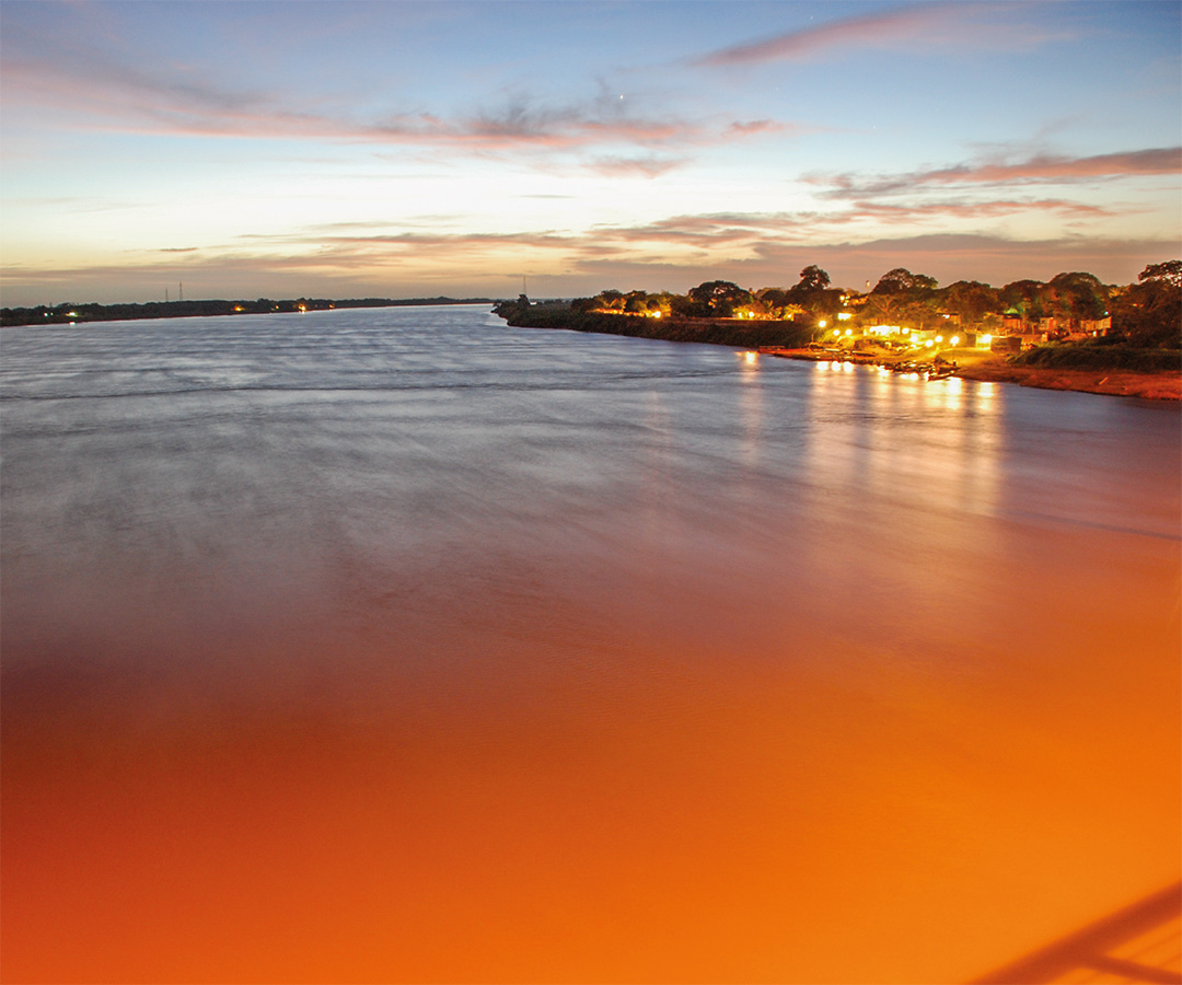 Río al atardecer con luces en la orilla.