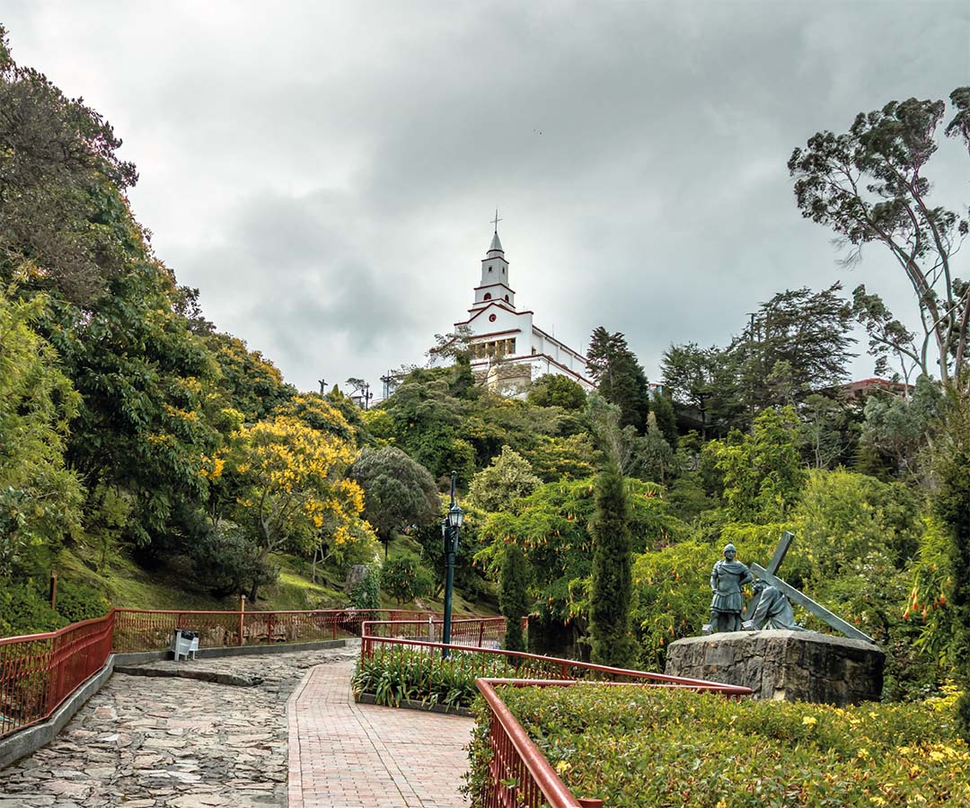 Camino hacia el Santuario de Monserrate en Bogotá, rodeado de vegetación exuberante y esculturas religiosas.