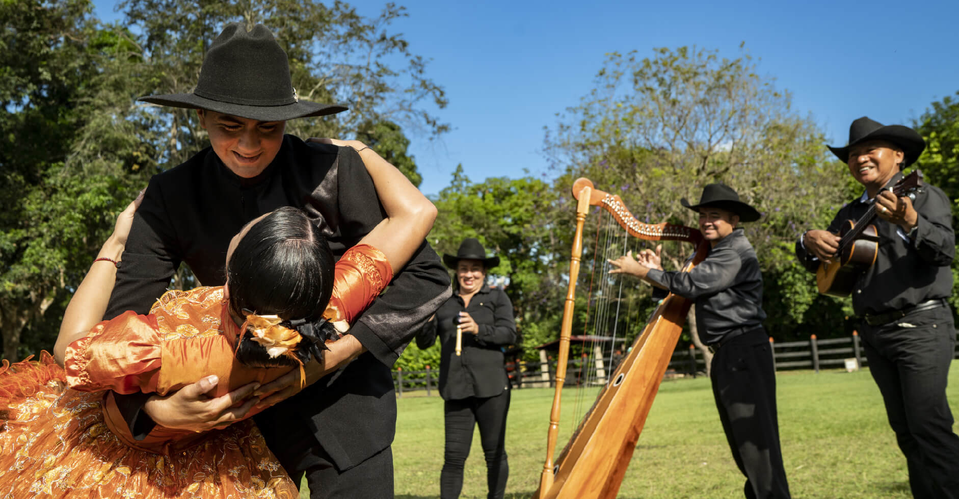 Pareja bailando joropo en un ambiente al aire libre, con músicos vestidos de negro tocando arpa.