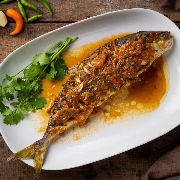 Plato de bocachico viudo servido con salsa criolla, acompañado de cilantro fresco y chiles como guarnición.