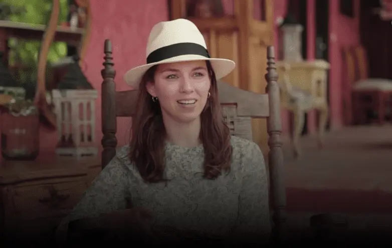 Mujer joven con sombrero blanco sentada en silla de madera en ambiente colonial