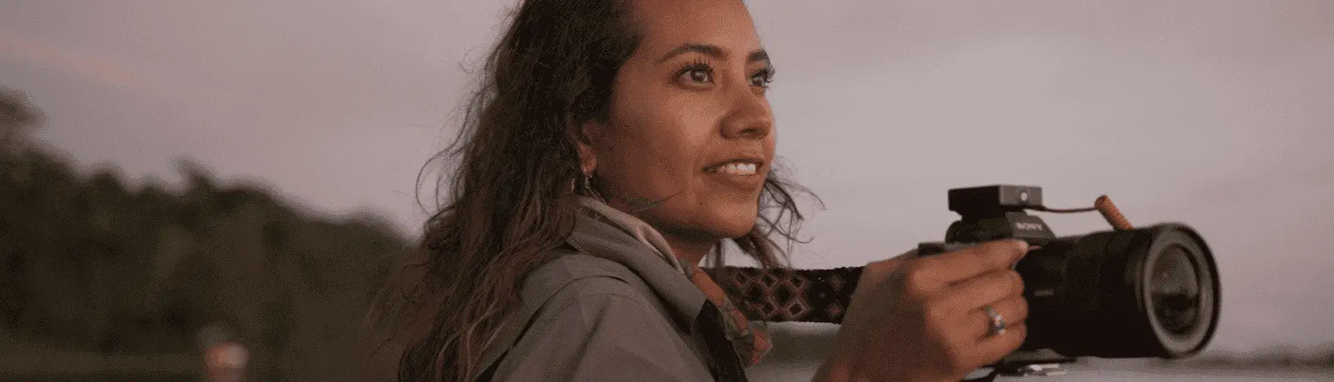 Mujer sosteniendo cámara profesional mientras observa el paisaje al atardecer