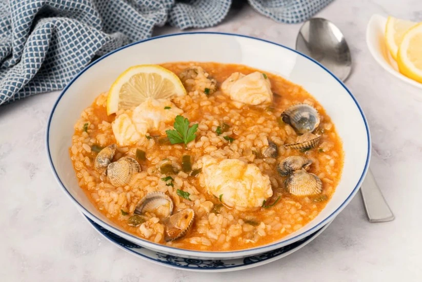 Plato hondo de arroz caldoso trozos de pescado, decorado con una rodaja de limón y perejil