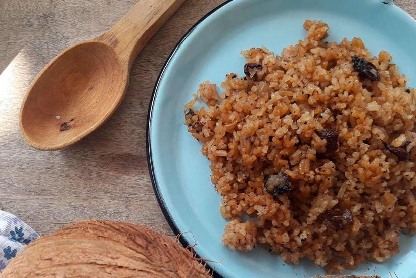 Plato de arroz con coco servido en un plato azul, acompañado de una cuchara de madera sobre una mesa 