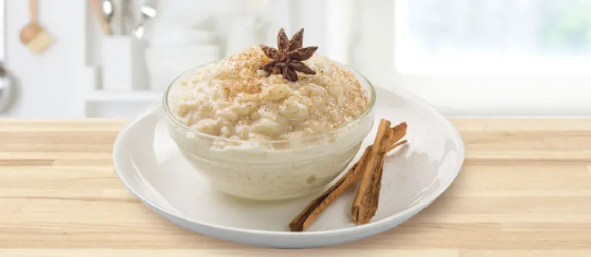 Arroz con leche, espolvoreado con canela y coronado con anís estrellado, con palitos de canela al lado, en un plato blanco