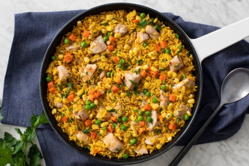 Arroz con pollo ervido en una cazuela negra, acompañado de rodajas de tomate y aguacate