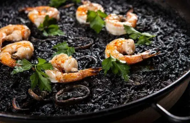 Arroz negro con camarones salteados y perejil fresco en sartén de hierro.