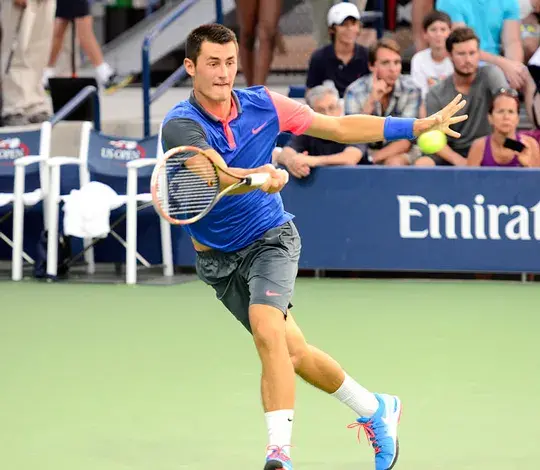 Tenista Bernard Tomic golpeando la pelota de revés durante un partido en una cancha verde.