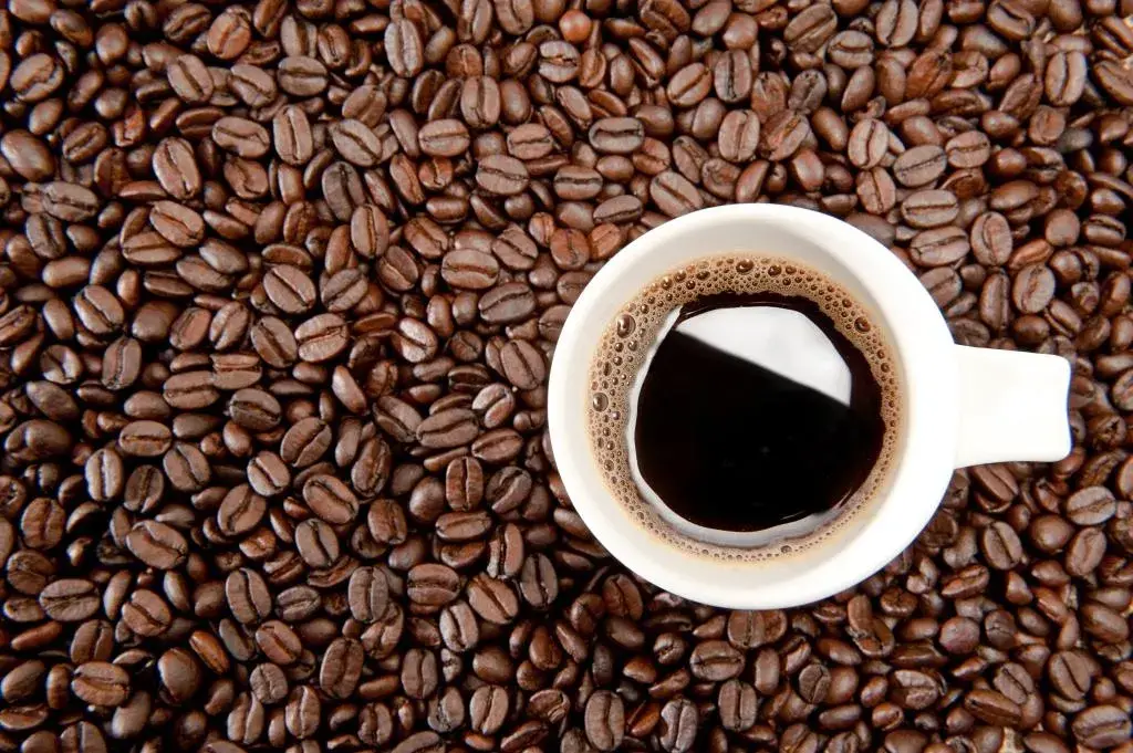 Taza de café oscuro rodeada de granos de café tostados.