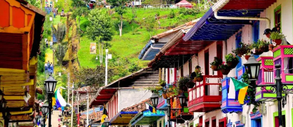 Casas coloridas de pueblo con balcones y una colina empinada.