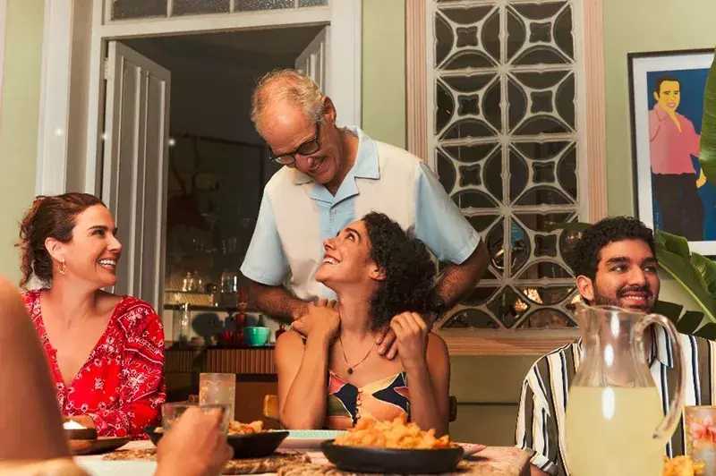 Hombre mayor dando masaje en los hombros a una joven en una cena familiar.