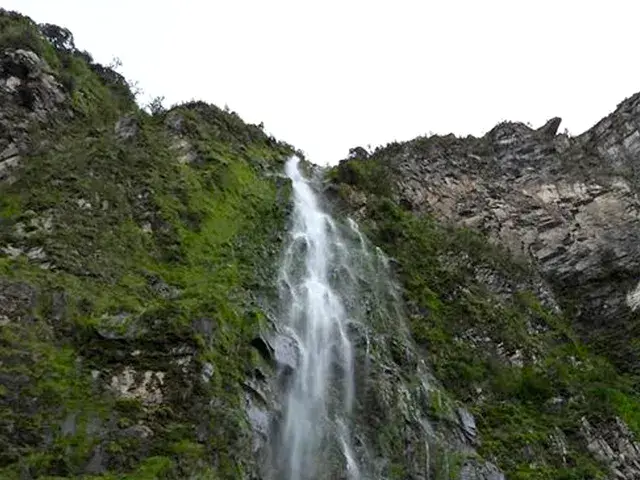 Cascada alta y delgada bajando por rocas cubiertas de musgo.