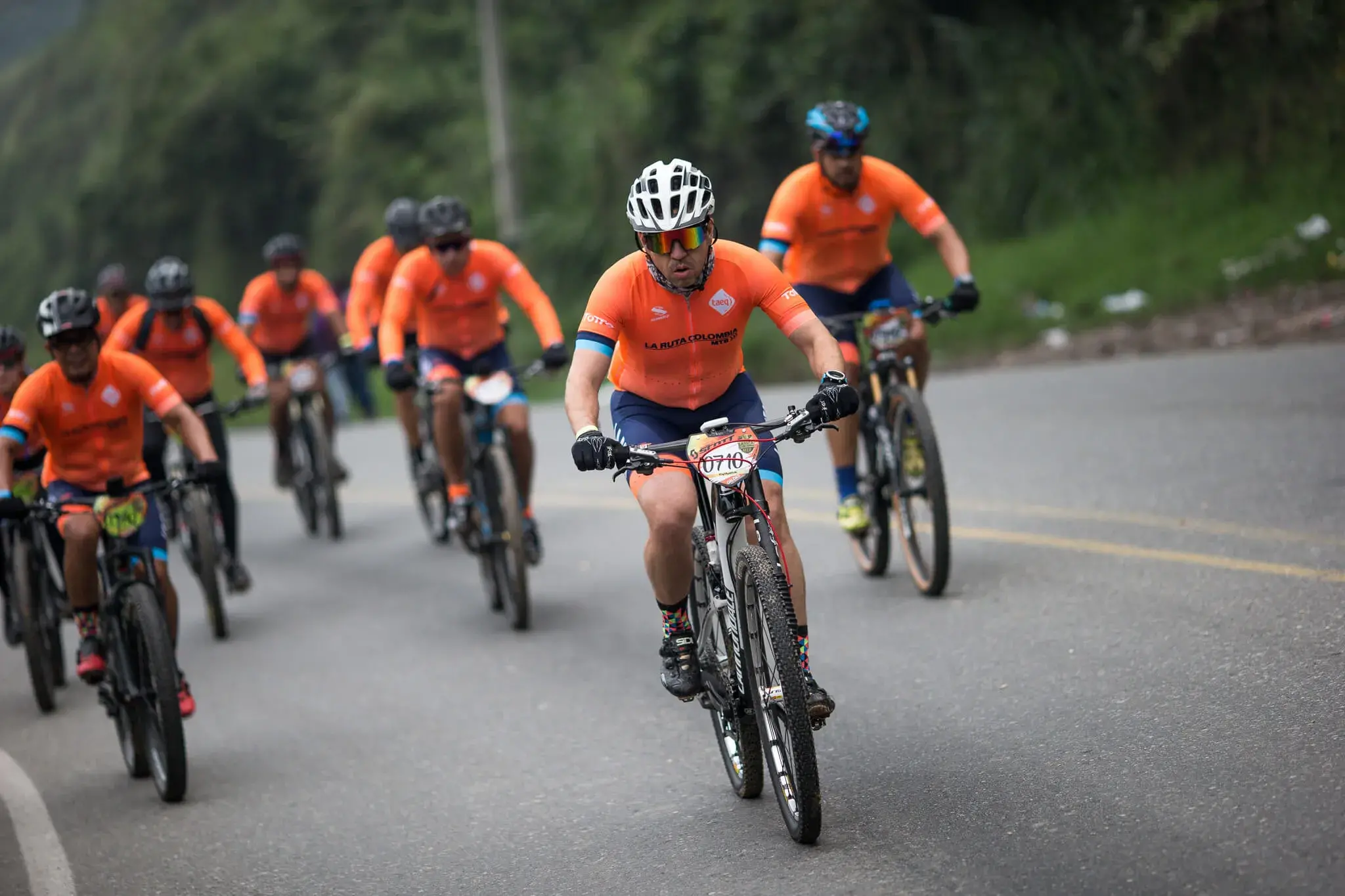 Ciclistas con uniformes naranjas de la Ruta Colombia pedaleando en grupo.