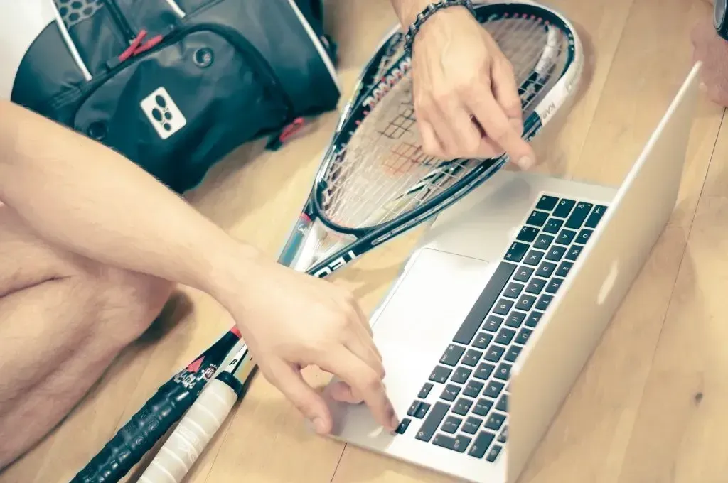 Jugadores de tenis revisando estrategia en portátil junto a raquetas.