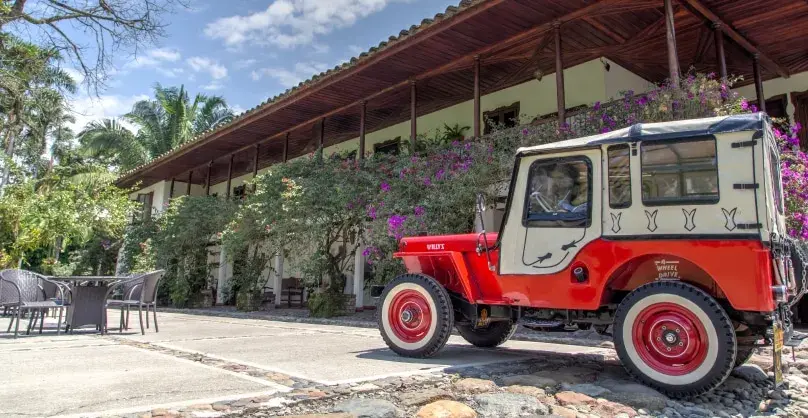 Jeeps Willys rojo y blanco estacionado frente a una hacienda.