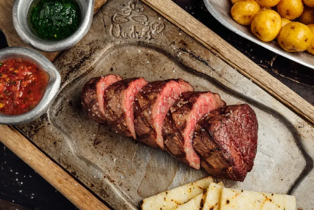 Lomo de res asado servido en rodajas con papas criollas y salsas típicas.