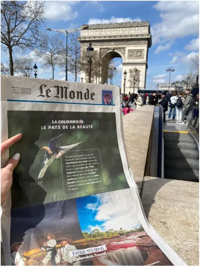 Mano sostiene periódico Le Monde sobre Colombia frente Arco del Triunfo.
