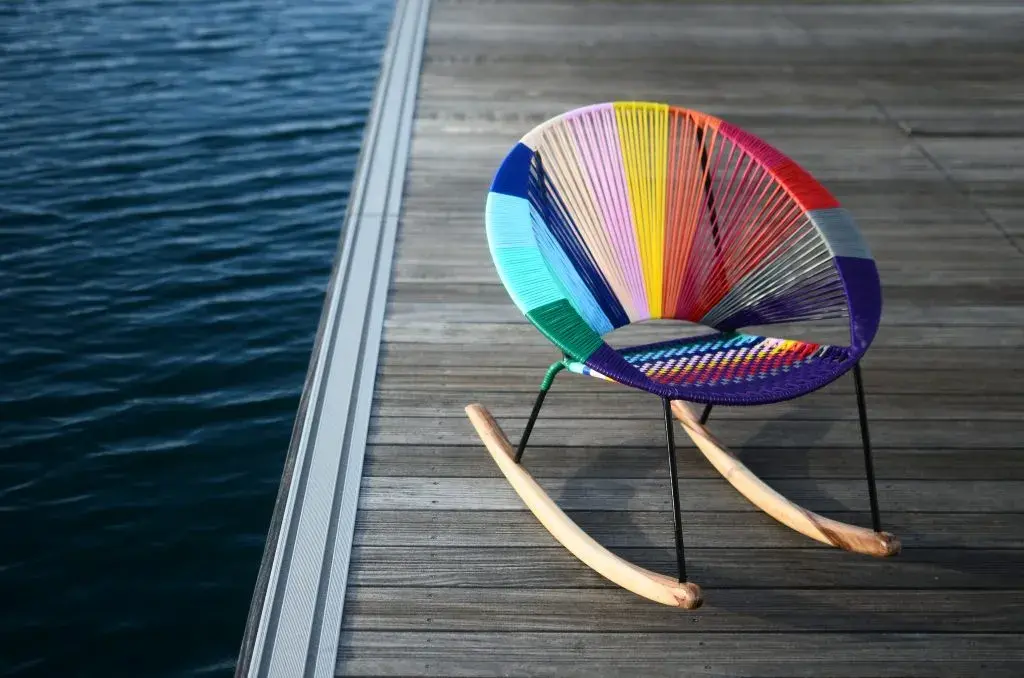 Mecedora Acapulco colorida sobre muelle de madera junto al agua.