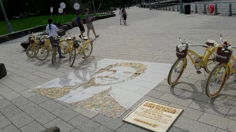 Mosaico de rostro en el suelo junto a bicicletas con mensaje de paz de Colombia