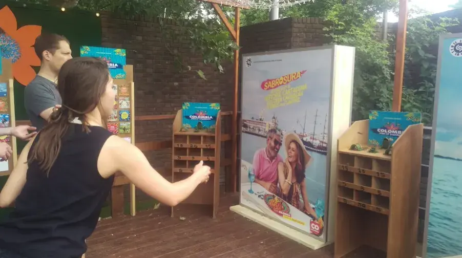 Mujer jugando bolirrana (rana) en un puesto promocional de turismo colombiano al aire libre.
