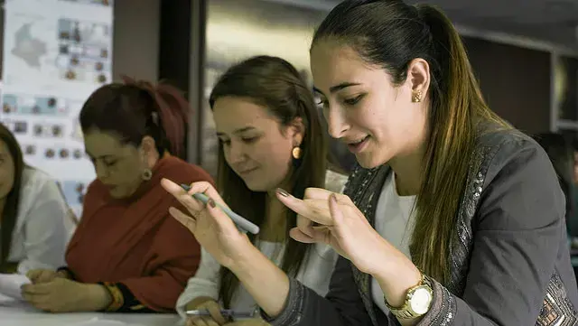 Cuatro mujeres sentadas en una mesa, la del frente señala con los dedos mientras sonríe.