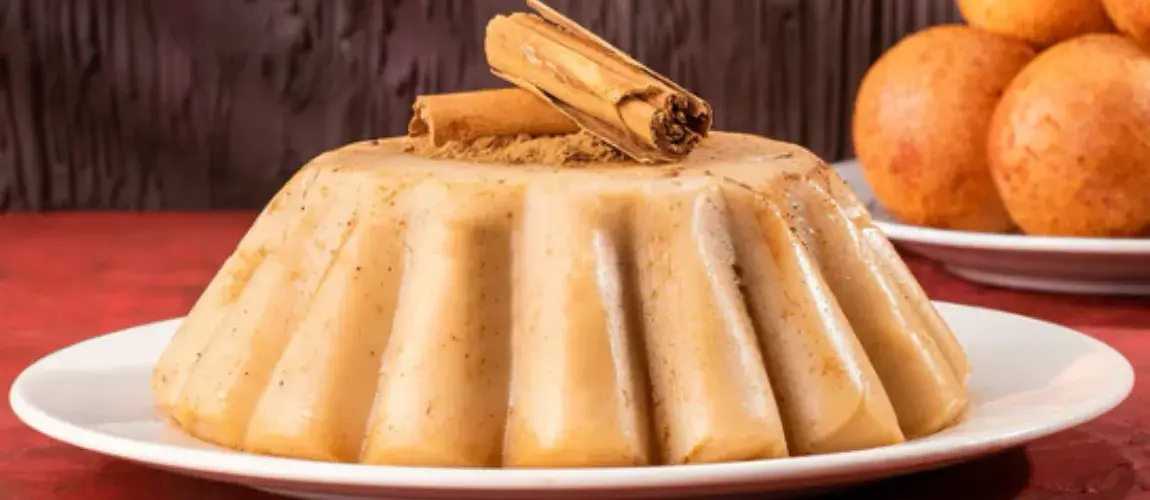 Porción de natilla colombiana con forma de molde, adornada con canela en rama y servida