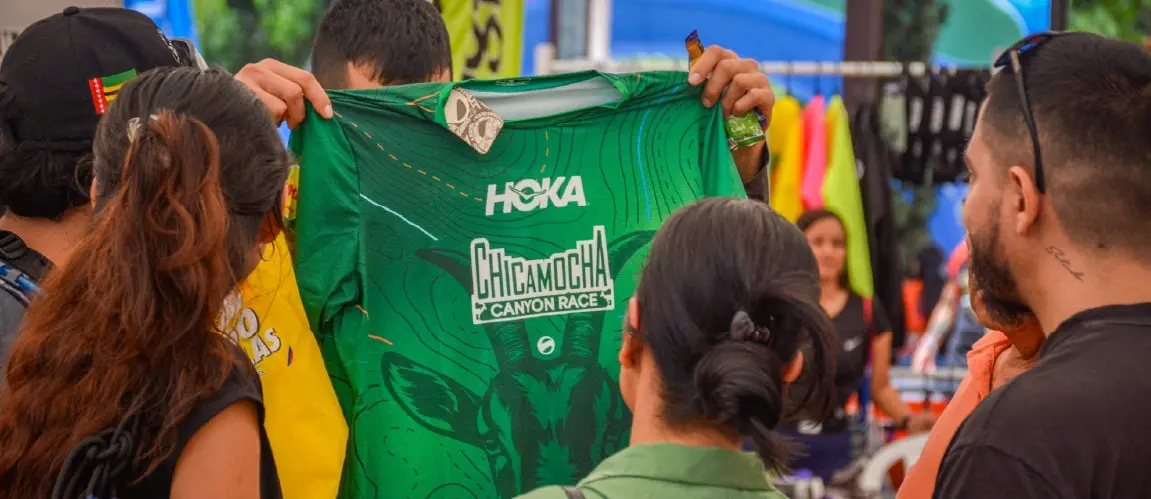 Persona mostrando camiseta oficial verde de la Chicamocha Canyon Race frente a otros asistentes