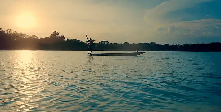Pescador de pie en una canoa, navegando un río al atardecer en Colombia.