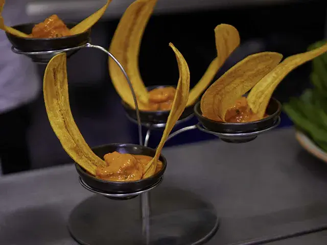 Platillo gourmet con plátanos fritos y salsa en un soporte metálico.