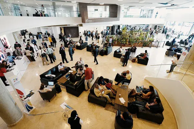 Vestíbulo amplio de convención, con gente conversando y sentada en sofás de cuero.