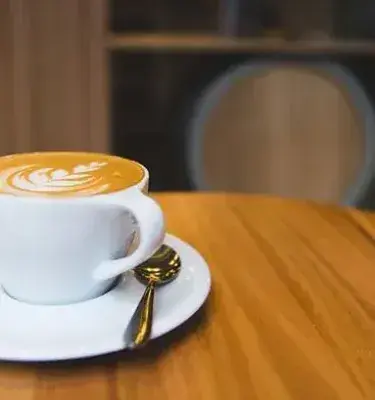 Coffee cup with latte art and spoon on wooden table.
