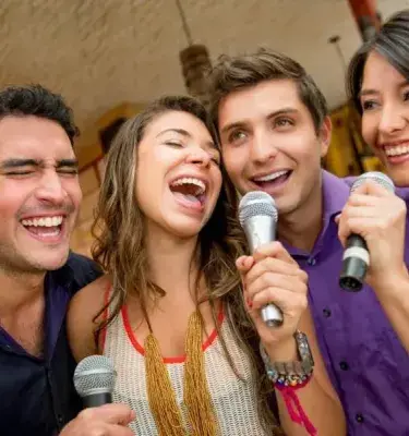 Cuatro amigos sonriendo y cantando karaoke con micrófonos.