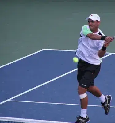 Tenista colombiano, Alejandro Falla, golpeando la pelota de revés en una cancha azul al aire libre.