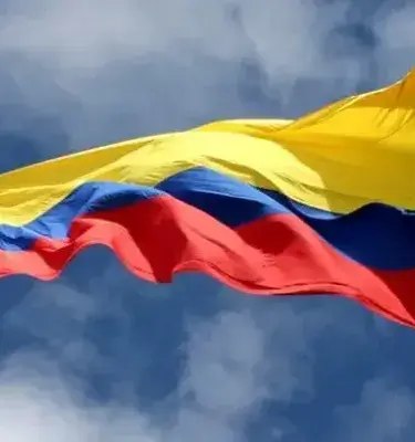 Colombian flag fluttering in the wind over a blue sky with clouds.