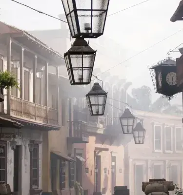 Calle antigua con balcones de madera y faroles colgantes, con ambiente de neblina que evoca un pueblo tradicional latinoamericano.