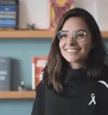 Retrato de Sofía Gómez luciendo gafas y un suéter negro con fondo de estantería con libros