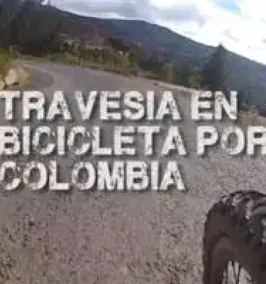 Carretera de tierra desde una bicicleta, con montañas de fondo y el texto "TRAVESÍA EN BICICLETA POR COLOMBIA".