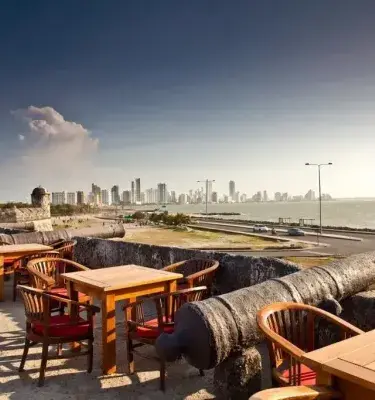 Mesas y sillas en un baluarte con cañón y vista a Cartagena.
