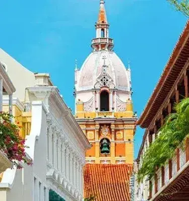 Calle colonial de Cartagena, Colombia, con balcones de madera y la cúpula de la Catedral al fondo.