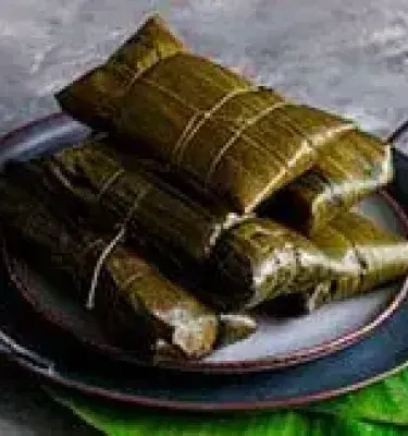 Envueltos tradicionales en hoja de plátano sobre plato rústico.