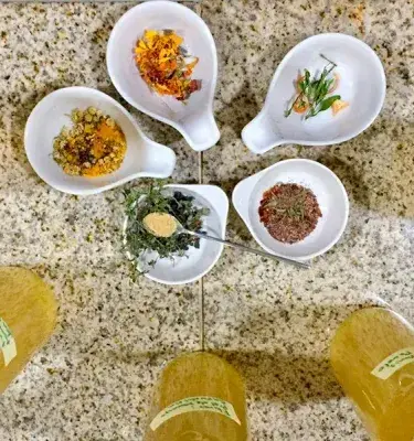 Five bowls with dried herbs and spices on a granite surface.