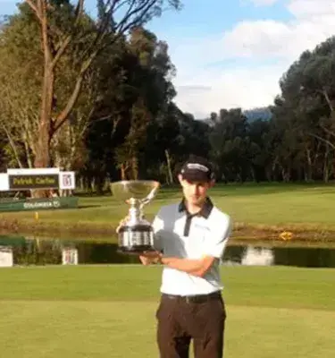 Golfista con trofeo en campo verde junto a estanque en día soleado.