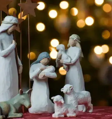 Figuras de pesebre navideño blanco: la Sagrada Familia y animales, con luces de fondo borrosas.