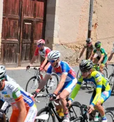 Grupo de ciclistas en competencia sobre calle adoquinada junto a muro antiguo