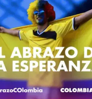 Hincha de fútbol con bandera y peluca de Colombia, con eslogan.