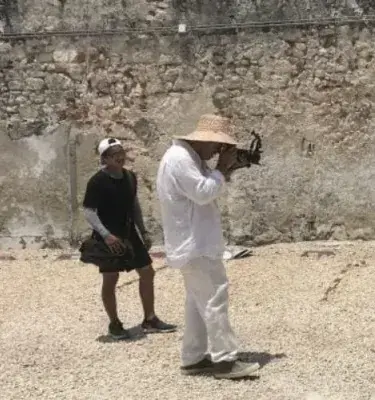 Hombre con sombrero grabando con cámara profesional junto a asistente en muro de piedra