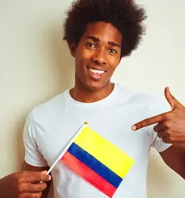 Hombre sonriente señalando una bandera de Colombia.