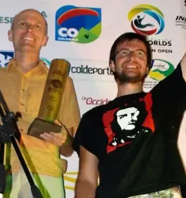Dos hombres con trofeo celebrando en un podio con un fondo de banners promocionales de Colombia.